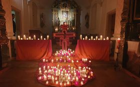 brennende Kerzen auf orange/gelben-Tüchern vor dem Taizekreuz in der Annabergkirche